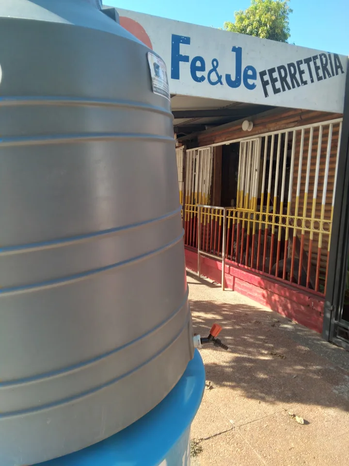 Cartel Fe y Je Ferretería sobre el portón, con un tanque de agua adelante