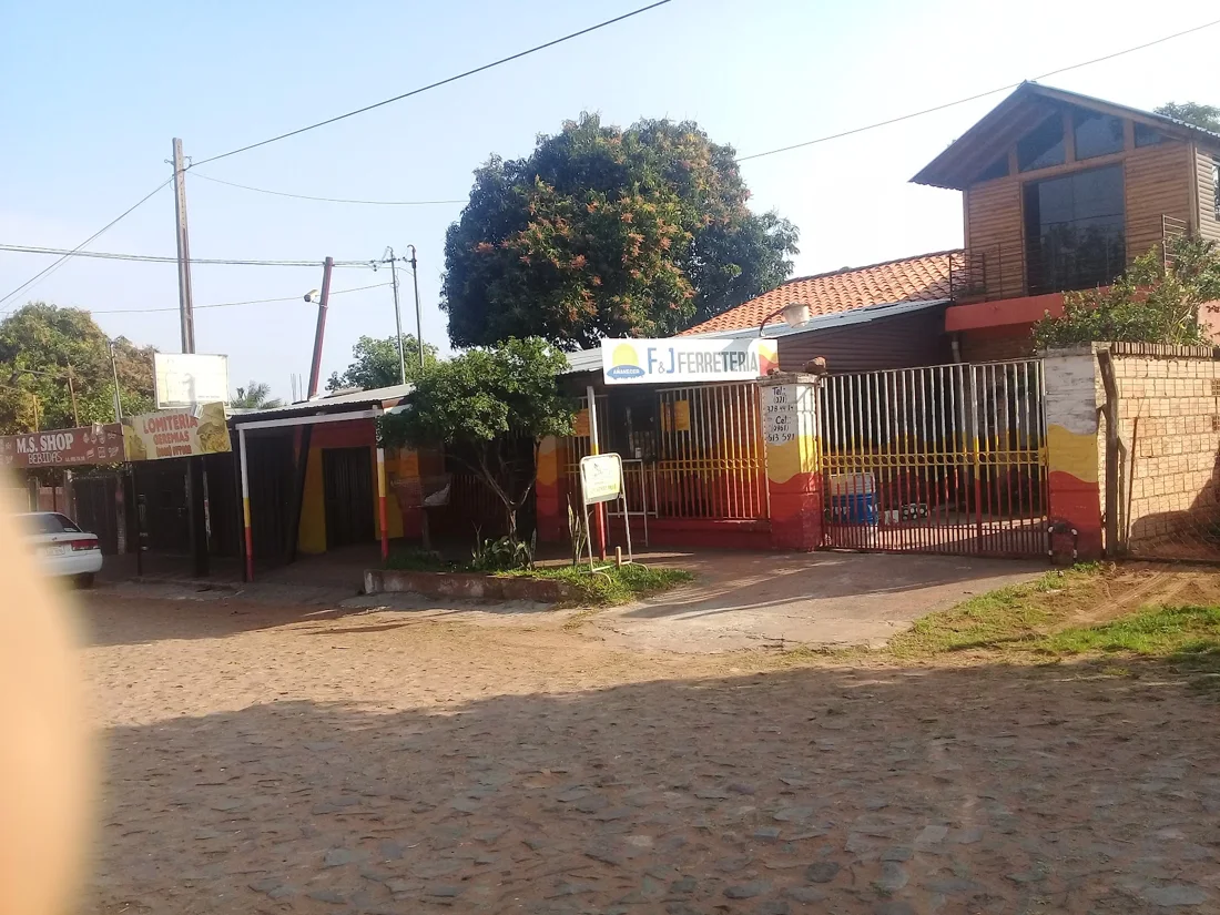 El frente de Fe y Je Ferretería en Villa Elisa: cartel blanco, portón de rejas rojo y amarillo, sobre calle empedrada